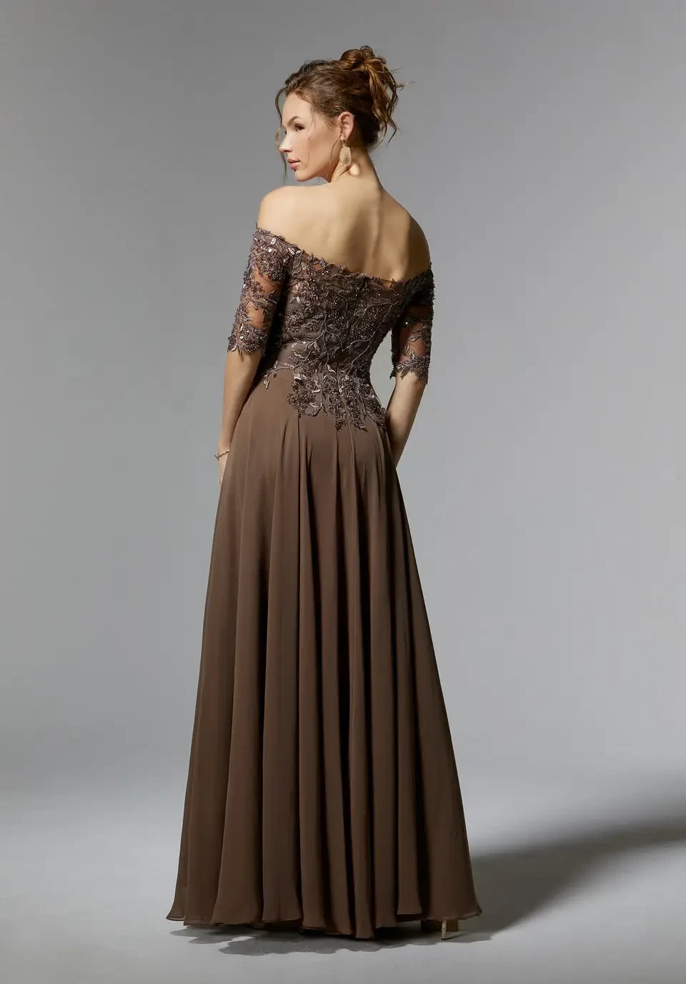 A woman in an elegant brown evening gown with off-the-shoulder sleeves and a thigh-high slit.