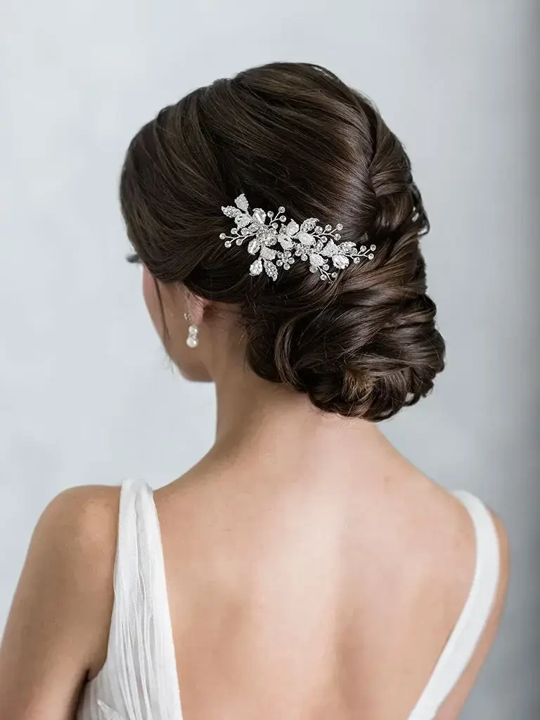 A woman with elegant, styled dark hair adorned with a decorative hairpiece and wearing a white dress, viewed from the back.