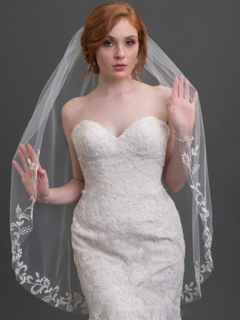 A woman in a strapless white wedding dress poses with her hands raised, wearing a long veil.