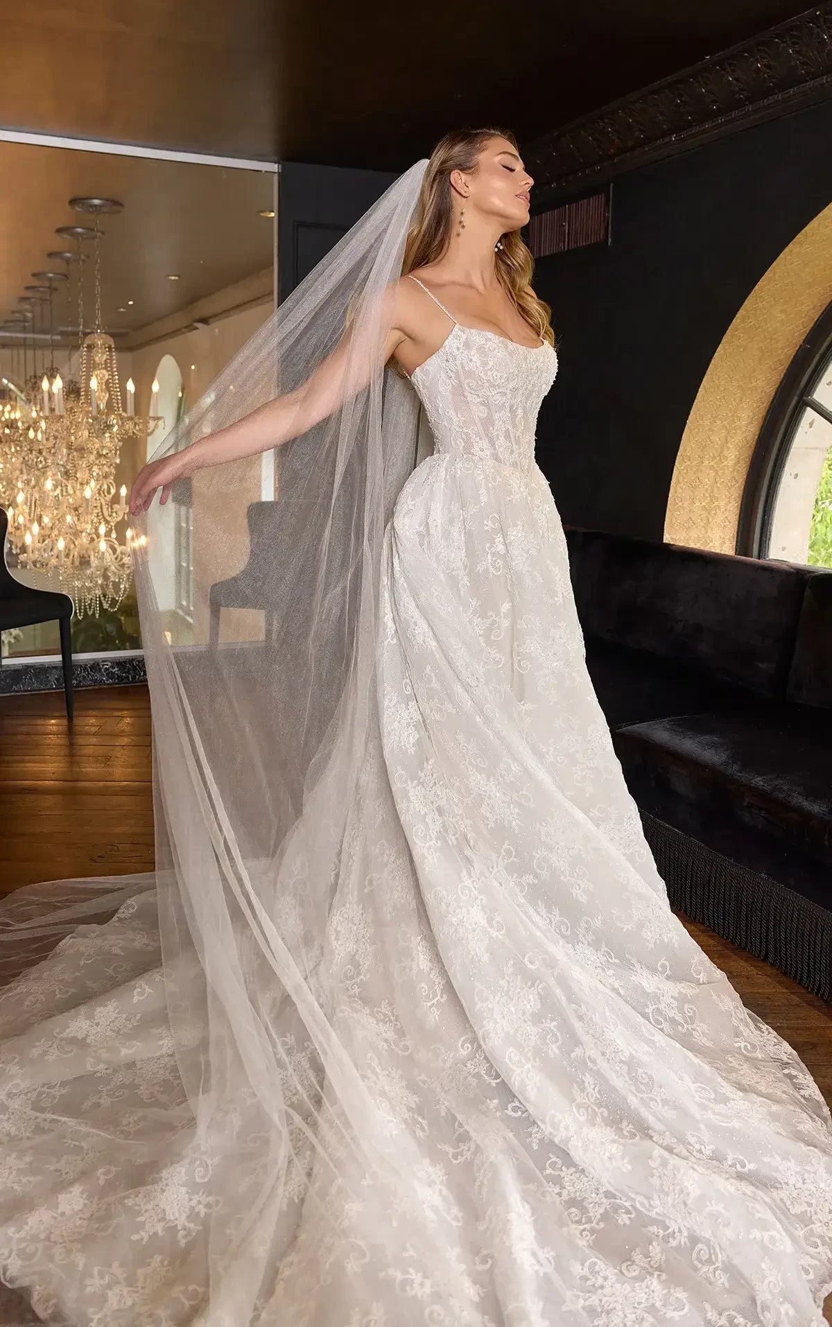 A bride wearing a beautiful white lace wedding dress with a long veil, posing gracefully in an elegant setting.
